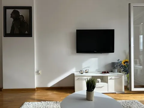Dio dnevne sobe sa televizorom na zidu, bijelom komodom i klub stolom. - image 8