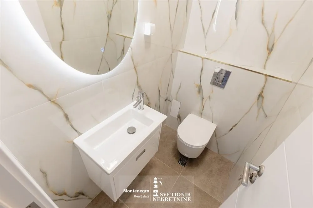 Moderne kupatilo opremljeno umivaonikom, WC šoljom i ogledalom sa pozadinskim osvjetljenjem.