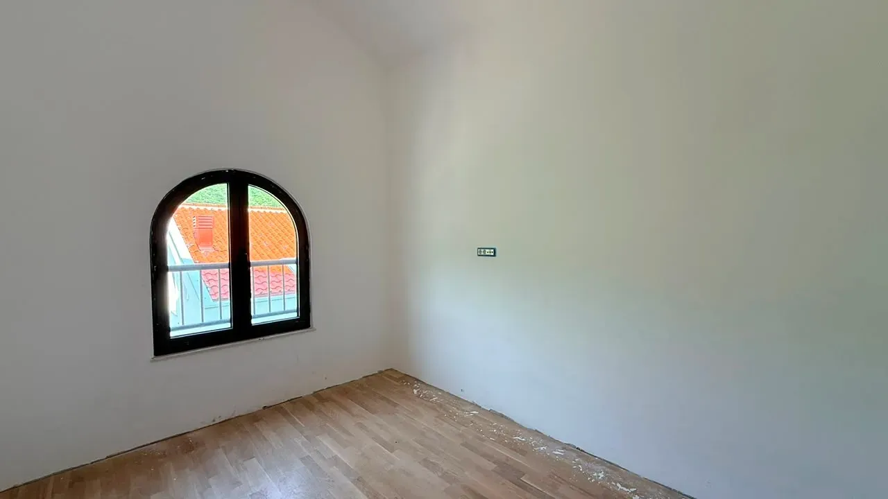Prazna prostorija sa drvenim podom i prozorom neobičnog oblika.