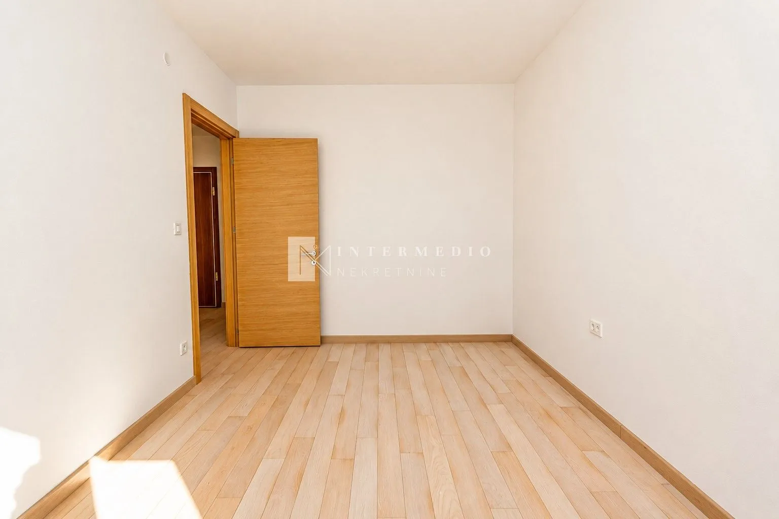 Prazna soba sa drvenim podom i otvorenim vratima.