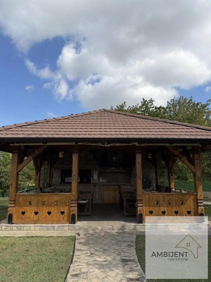 Drvena nadstrešnica sa roštiljem i garniturom za sedenje u dvorištu.