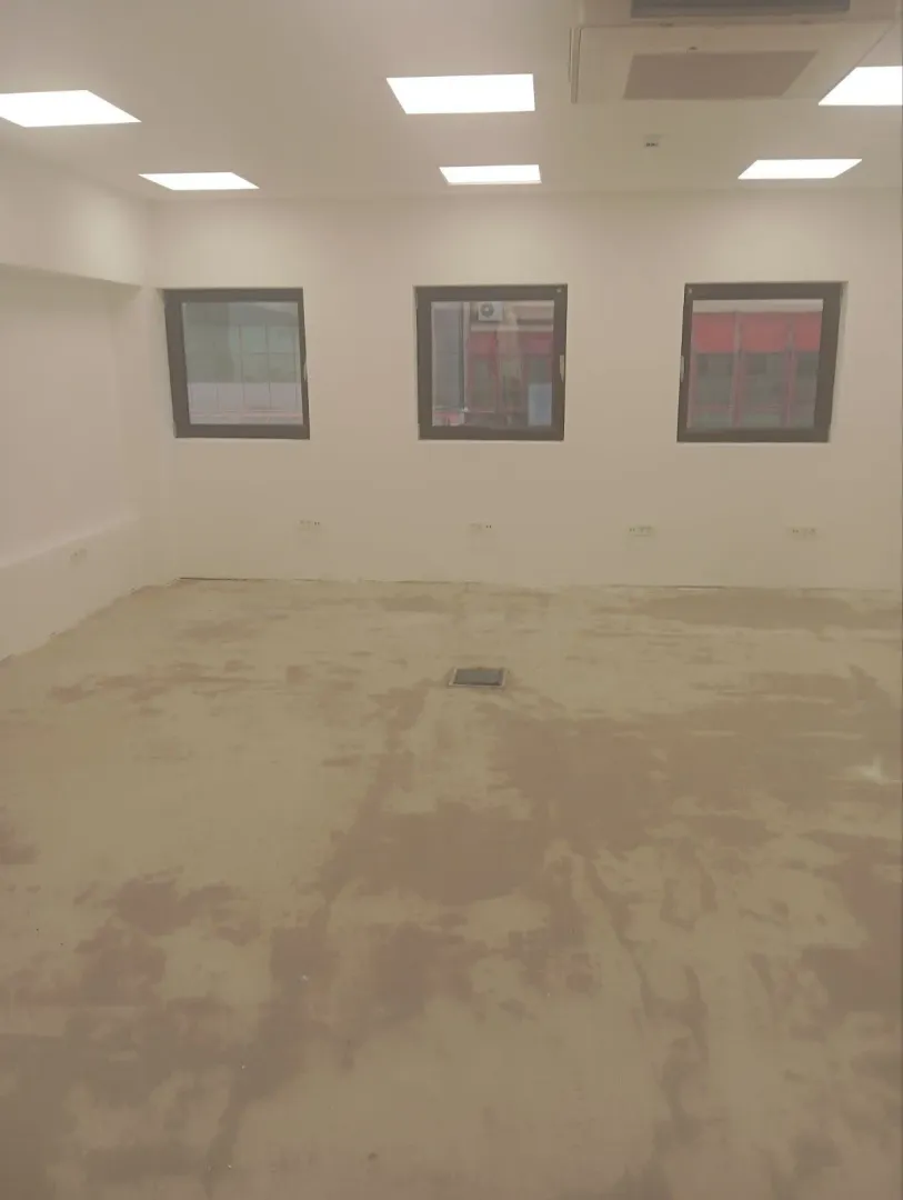 An empty unfinished room with recessed ceiling lights and three windows.