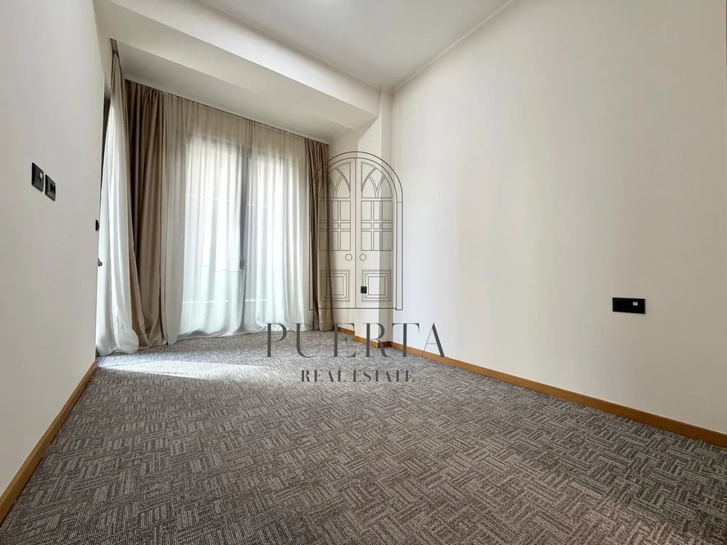 Empty room with carpeted flooring and balcony doors with curtains.