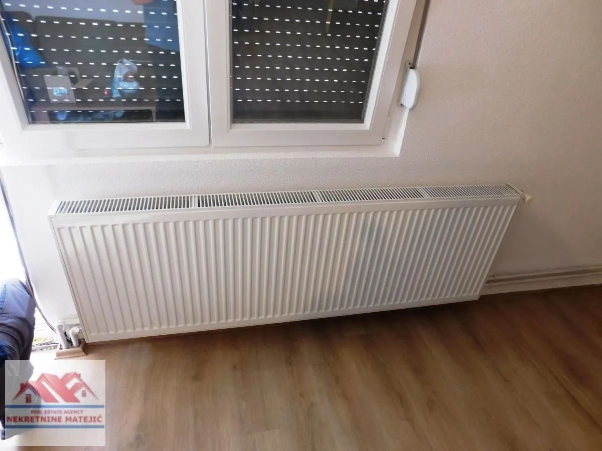 Radijator ispod prozora u sobi sa laminatnim podom.