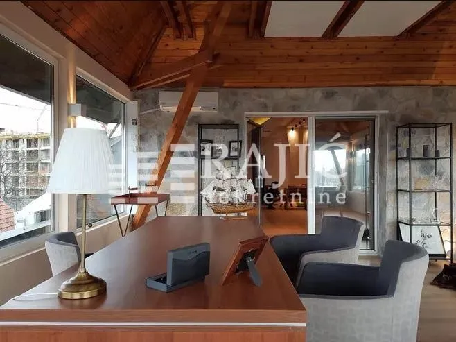 Living room with a desk, wooden ceiling and large windows.