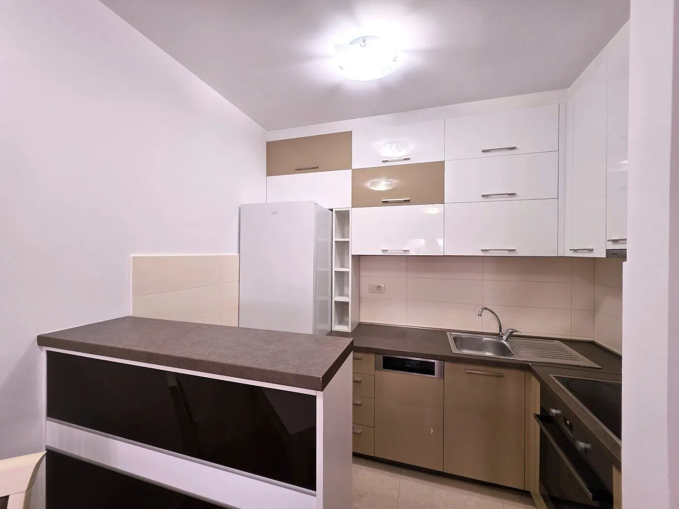 Smaller kitchen with white and beige units and a breakfast bar.