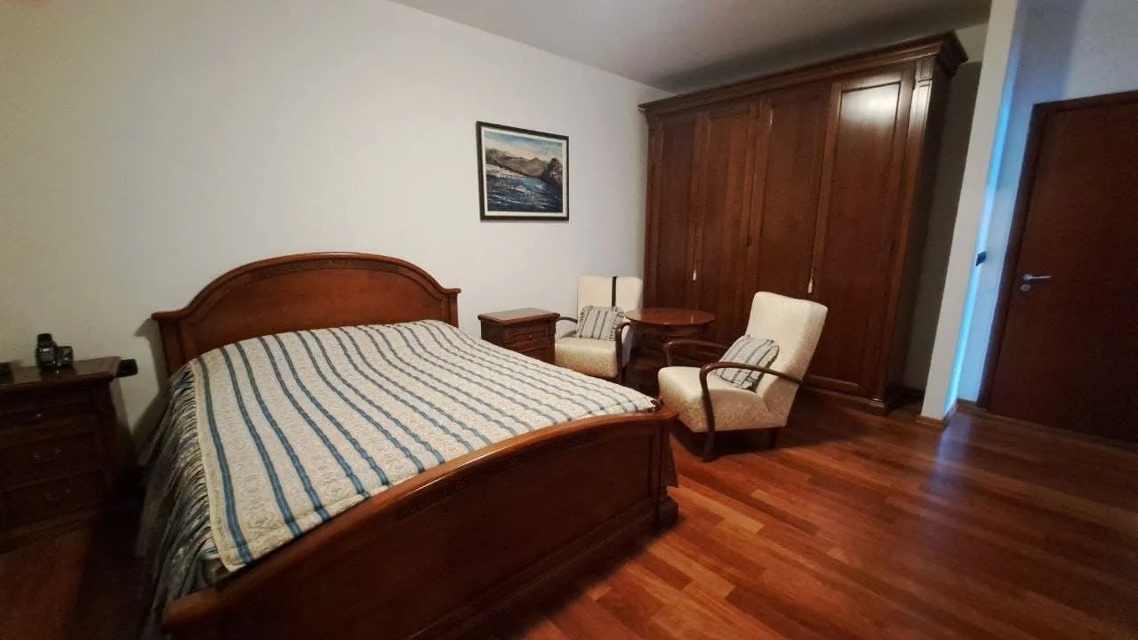 Spavaća soba sa bračnim krevetom, drvenim ormarom i foteljama.
