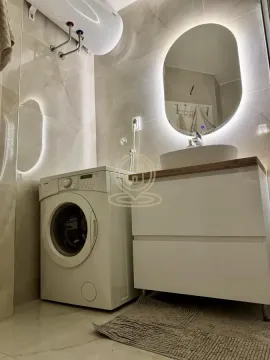 Bathroom with a vanity sink, backlit mirror, and washing machine. - image 16