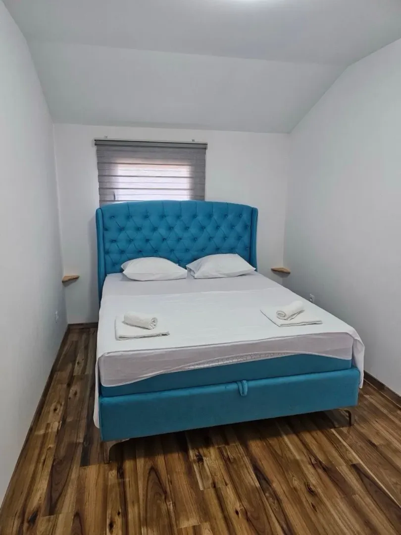 Bright bedroom with a large blue bed and wooden flooring.