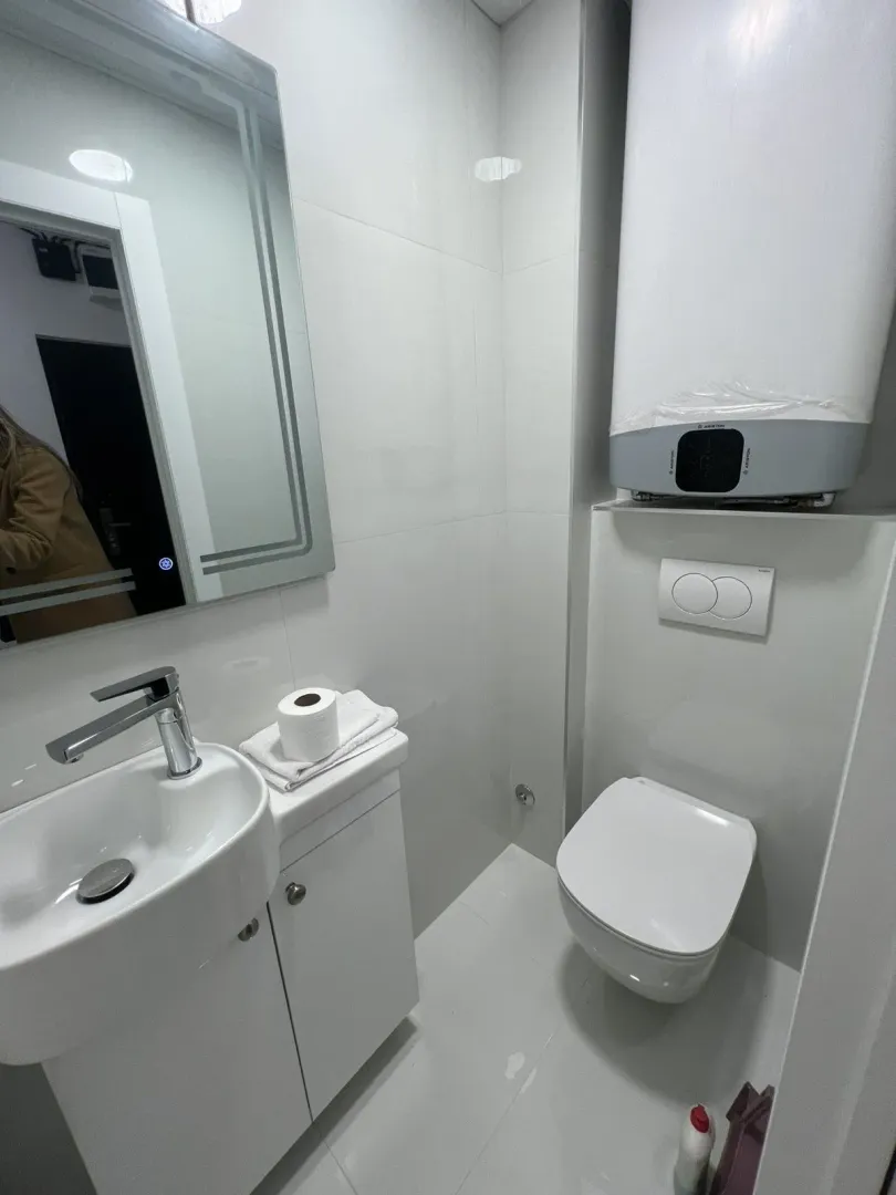 A modern and functional bathroom featuring white tiles, a sink, and a toilet.