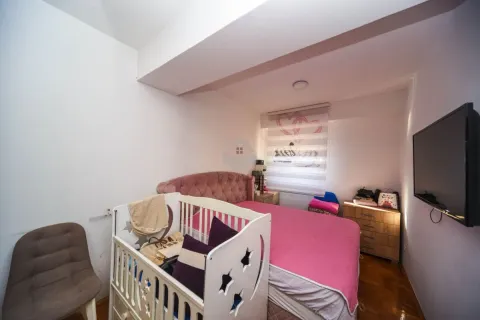 Spavaća soba sa krevetom, krevetcem za bebe, komodom i televizorom na zidu. - image 10