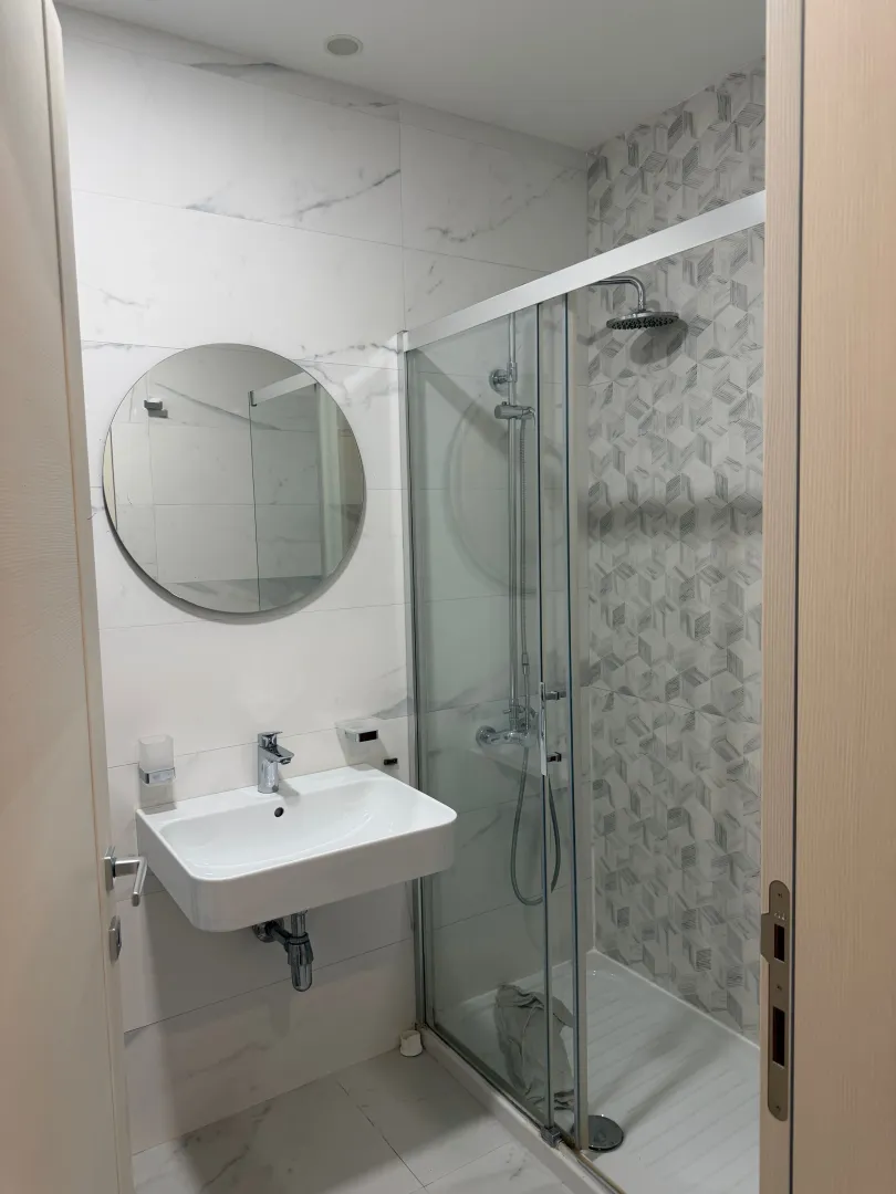 Modern bathroom with a washbasin, round mirror, and walk-in shower.