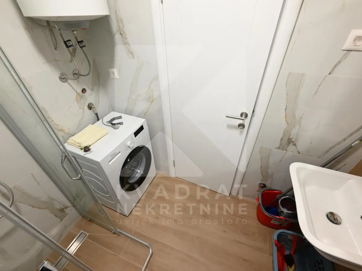Bathroom with a washing machine, washbasin, and marble-patterned tiles.