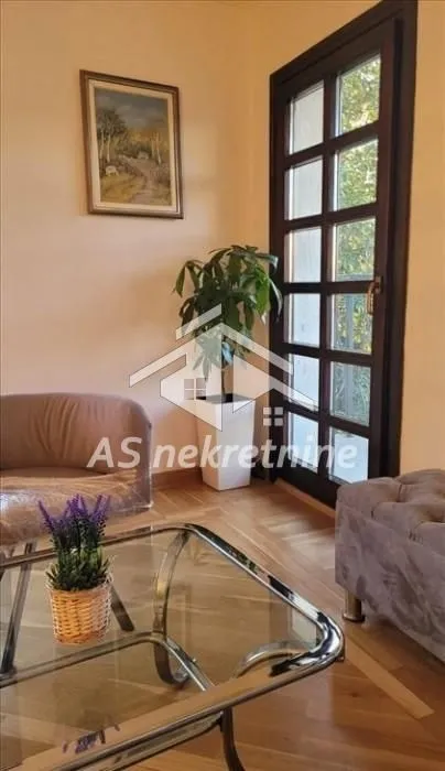 Dnevna soba sa garniturom, staklenim stočićem i balkonskim vratima.