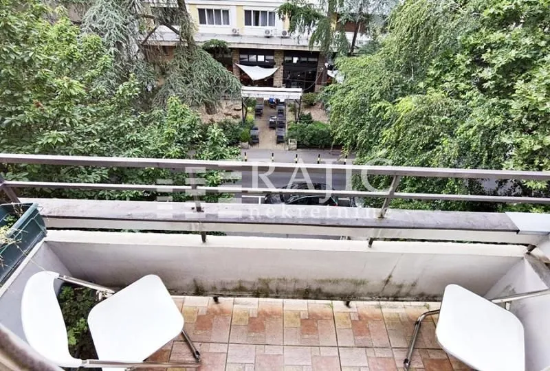 Small balcony with seating furniture and a view of greenery and the street.