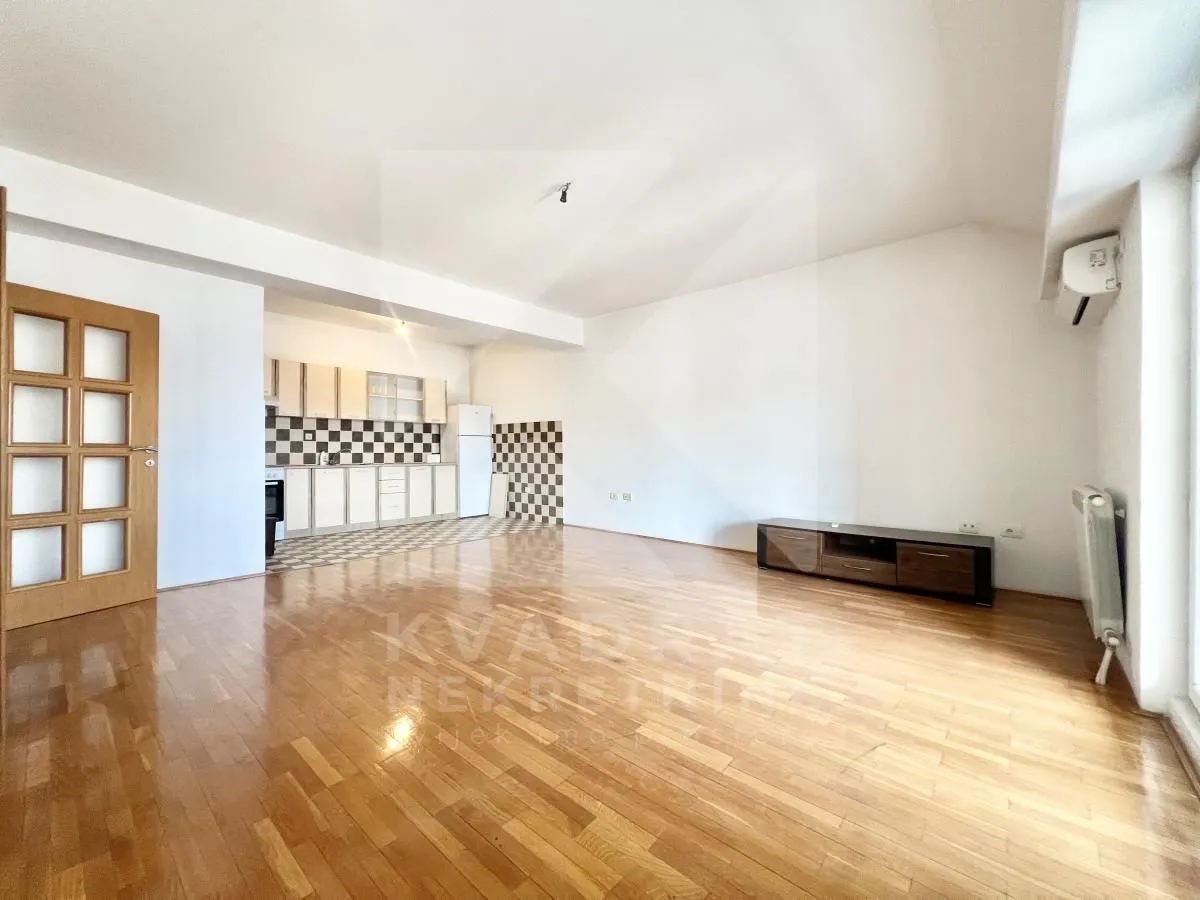 Spacious living room with wooden flooring and a kitchen in the background.