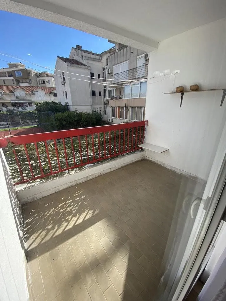 Covered balcony space with a red railing and a view of the neighborhood.