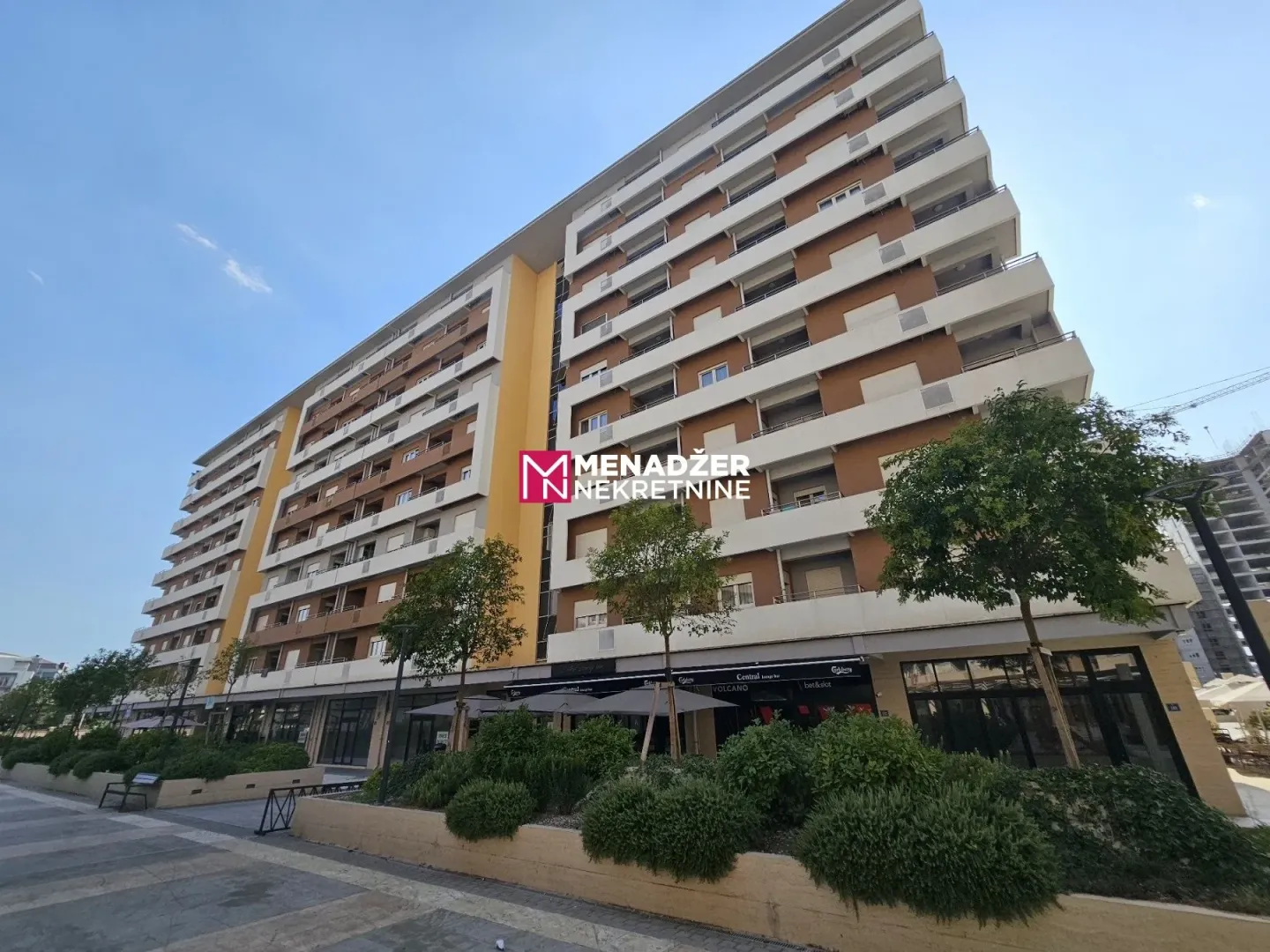 Pogled na spoljašnjost moderne višespratne stambene zgrade sa uređenim prizemljem i zelenilom.