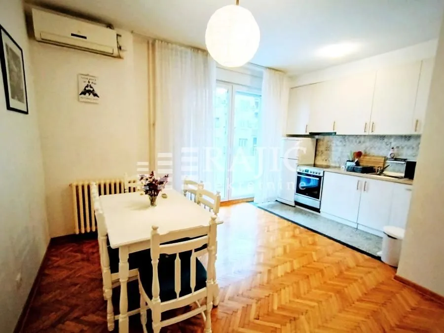 Dining area connected to a kitchen with white furniture and parquet flooring.