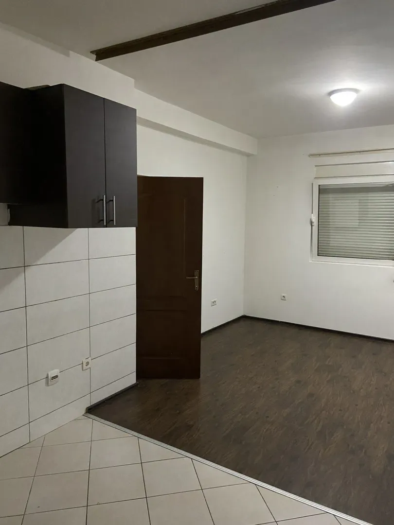Prazna prostorija sa tamnim podom i kuhinjskim elementom.