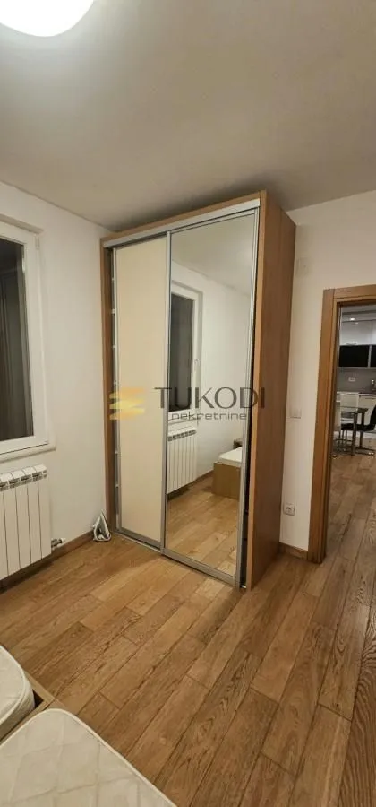 Manja spavaća soba sa velikim plakarom sa ogledalom i drvenim podom.