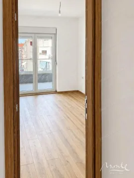 Pogled iz hodnika kroz vrata na praznu prostoriju sa drvenim podom i izlazom na terasu. - image 4