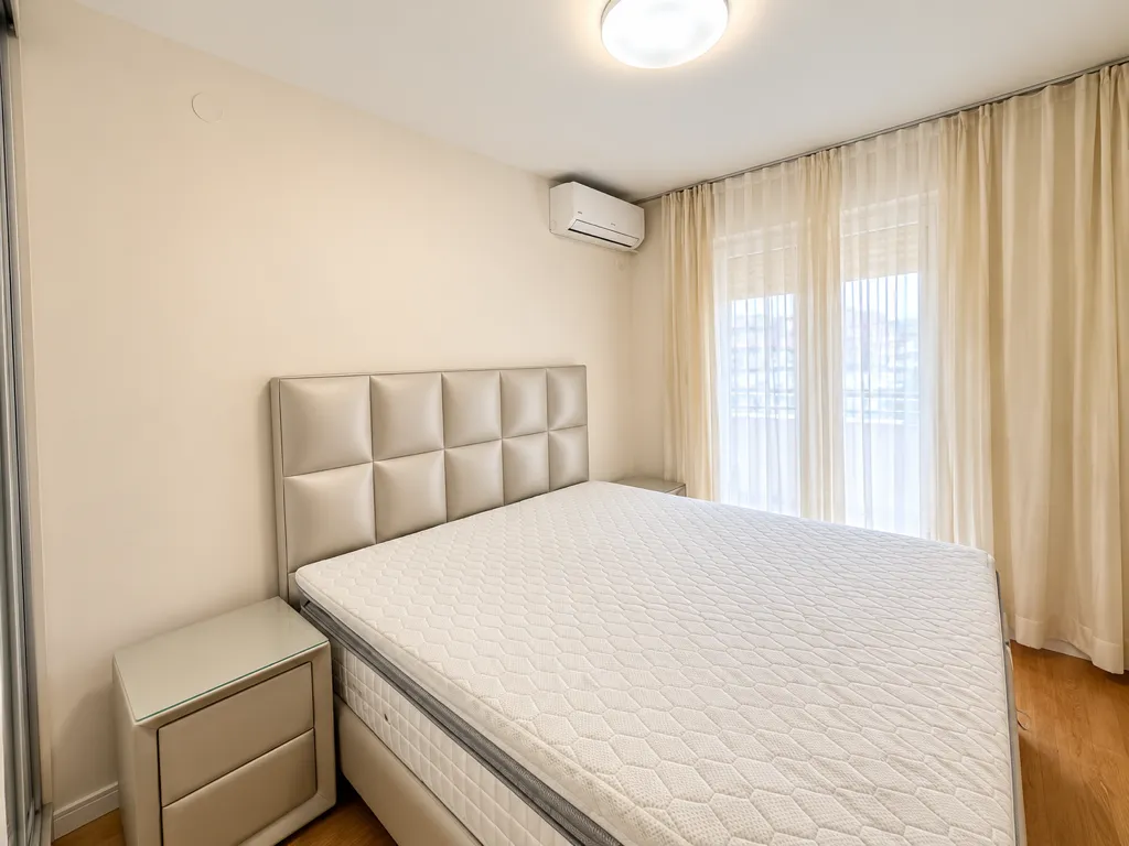 Bright bedroom with a double bed, nightstands, and air conditioning.