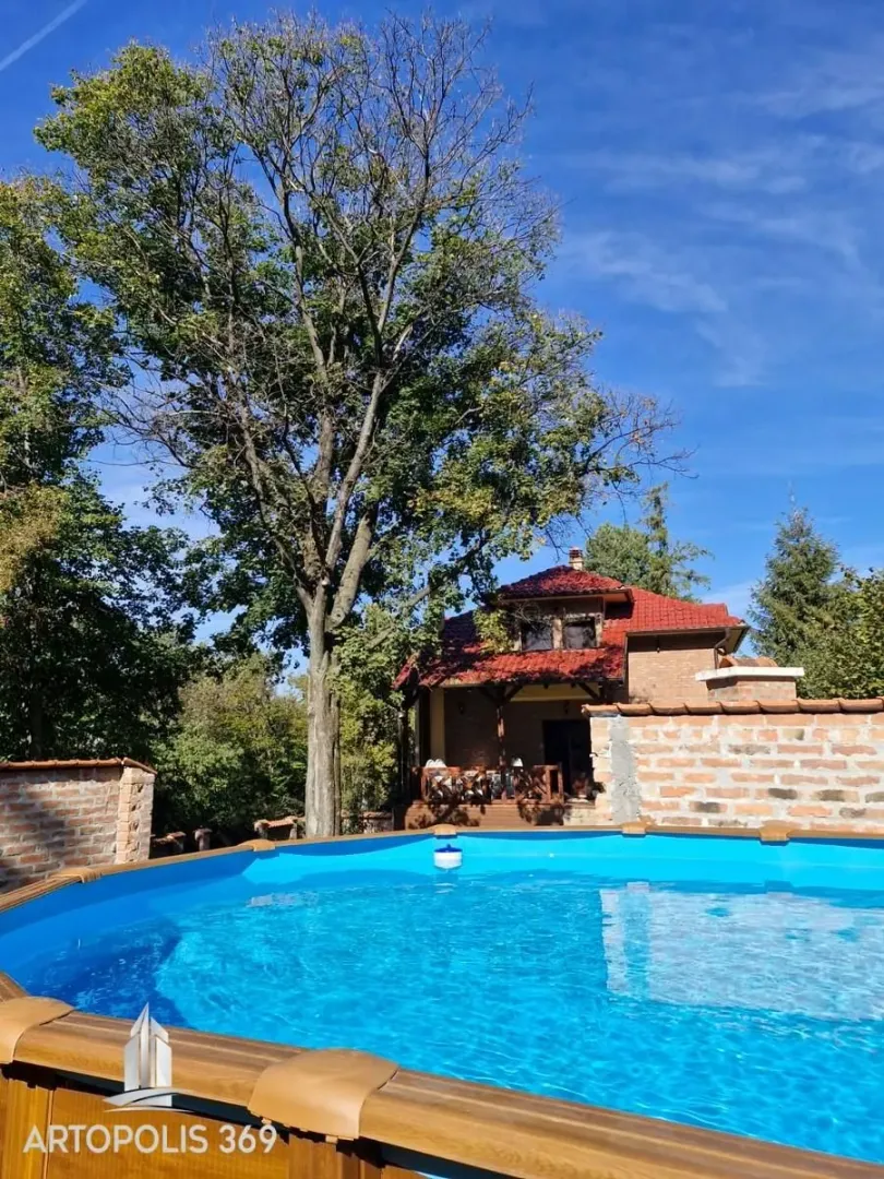 Pogled na bazen u dvorištu sa kućom i drvećem u pozadini.