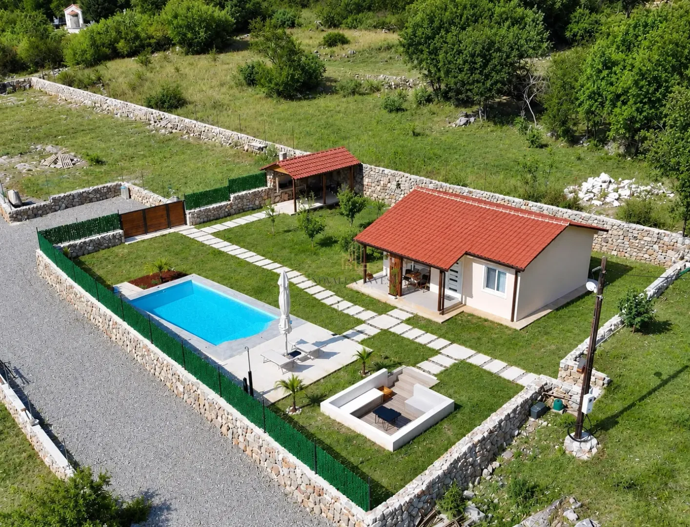 Aerial view of a house with a swimming pool and landscaped yard fenced with a stone wall.