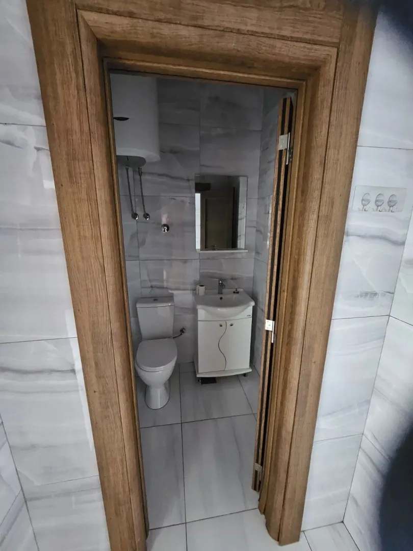 View of the tiled bathroom with sanitary ware through an open wooden door frame.