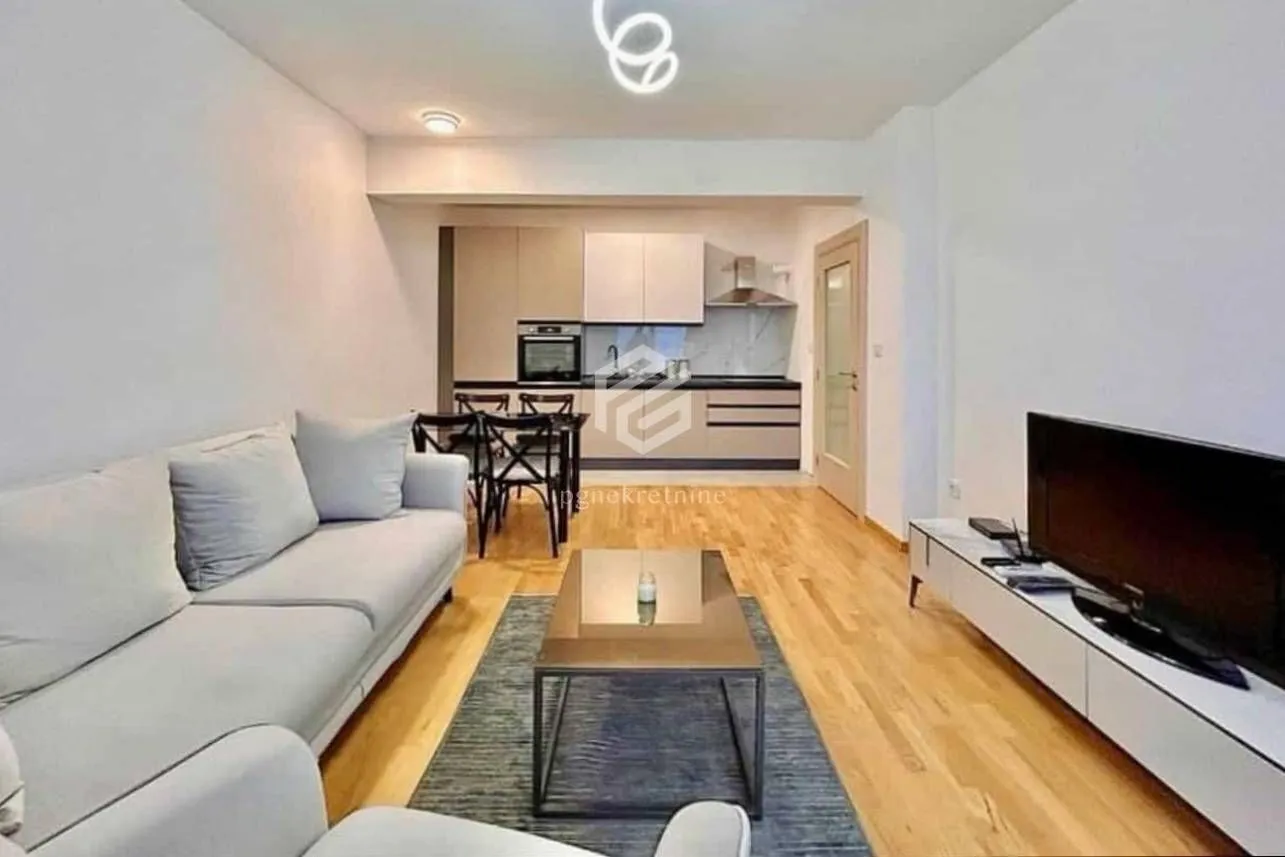 Living room with a sofa, TV, and a view of the dining area and kitchen in the background.
