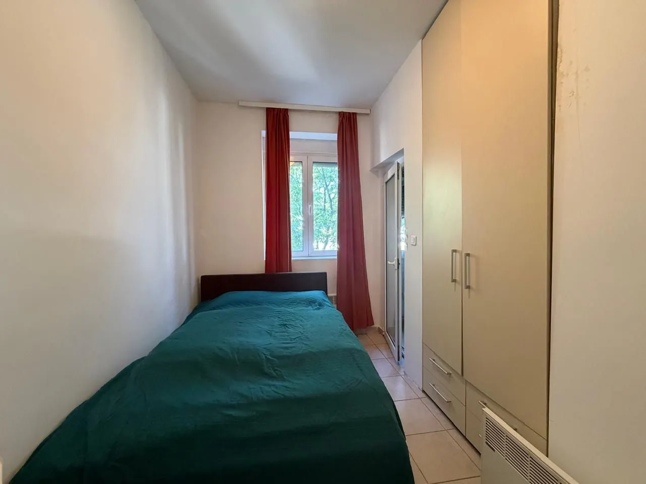 Manja spavaća soba sa krevetom, garderoberom i crvenim zavjesama.