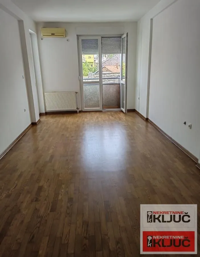 Prazna soba sa drvenim parketom i izlazom na balkon.