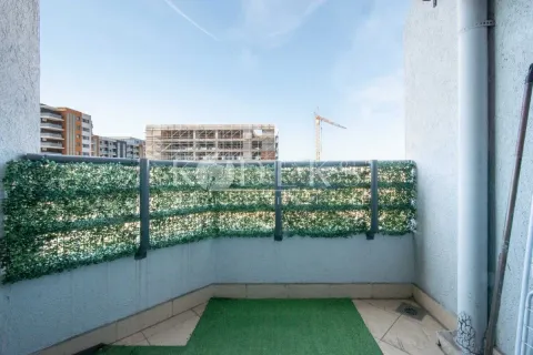 Manji balkon sa ogradom ukrašenom vještačkom travom i pogledom na okolne zgrade u izgradnji. - image 10