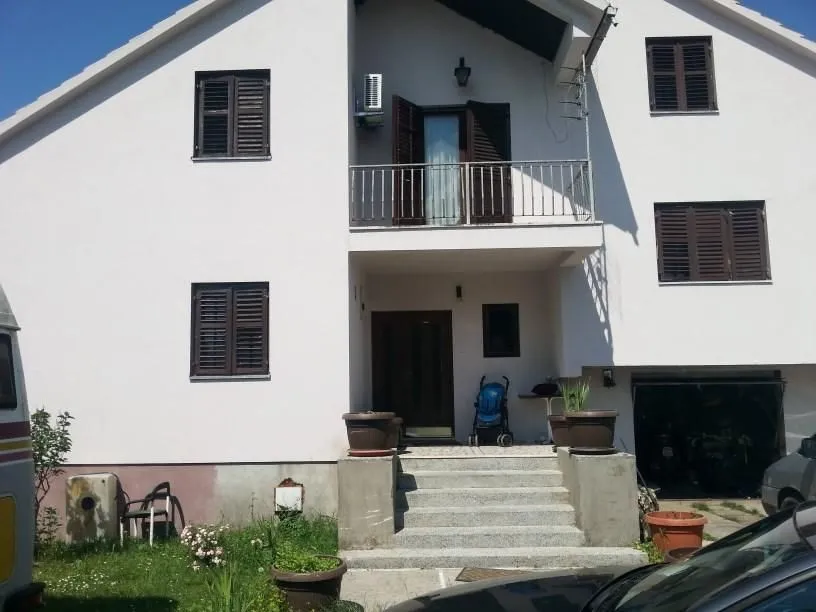 Dvospratna porodična kuća sa bijelom fasadom i tamnim prozorima.