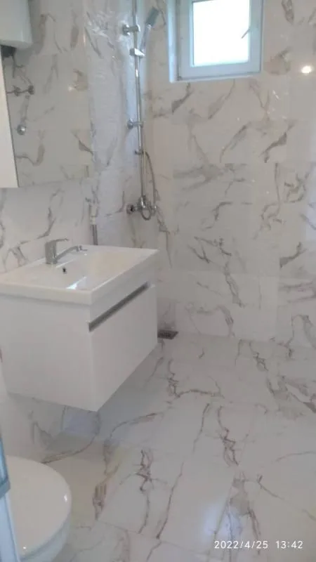 Modern bathroom equipped with a shower cabin, washbasin, and white ceramic tiles with marble patterns.