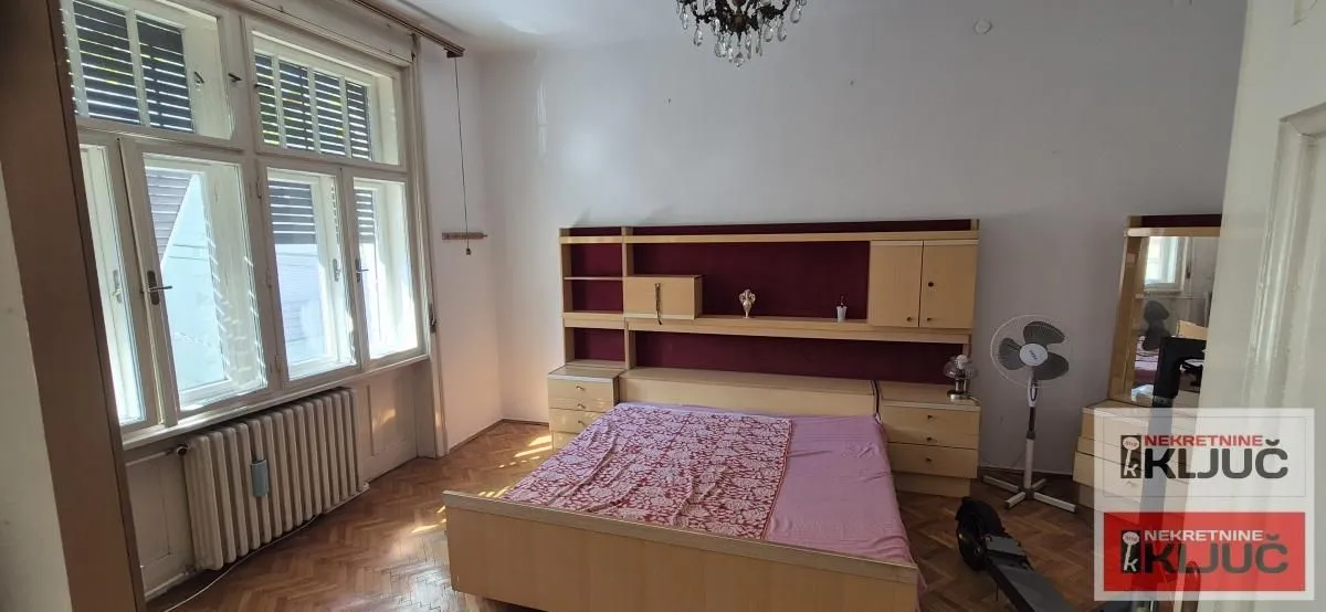 Nameštena spavaća soba sa velikim prozorima i drvenim podom.