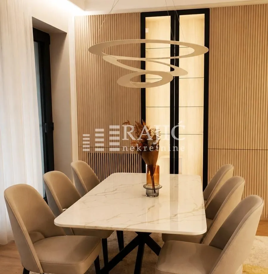 Modern dining room with a marble table, beige chairs, and a decorative chandelier.