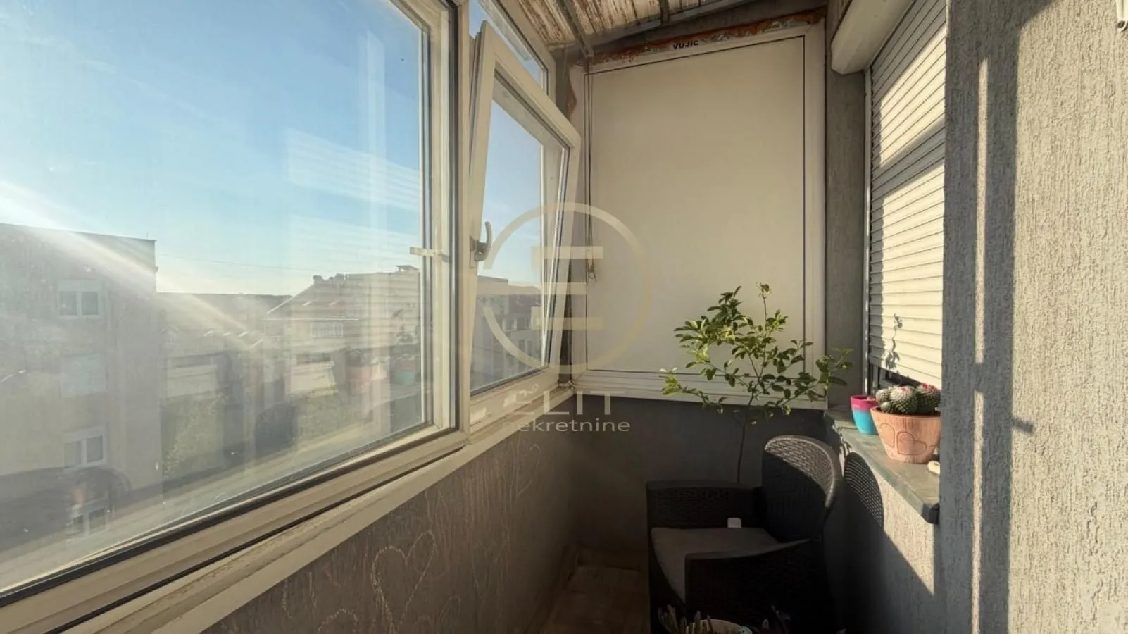 Zastakljeni balkon sa stolicom i saksijama sa biljkama.