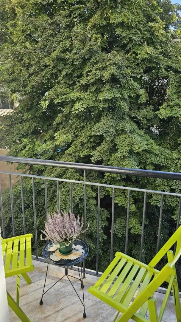 Balcony with green chairs, a small table, and a view of tree canopies.