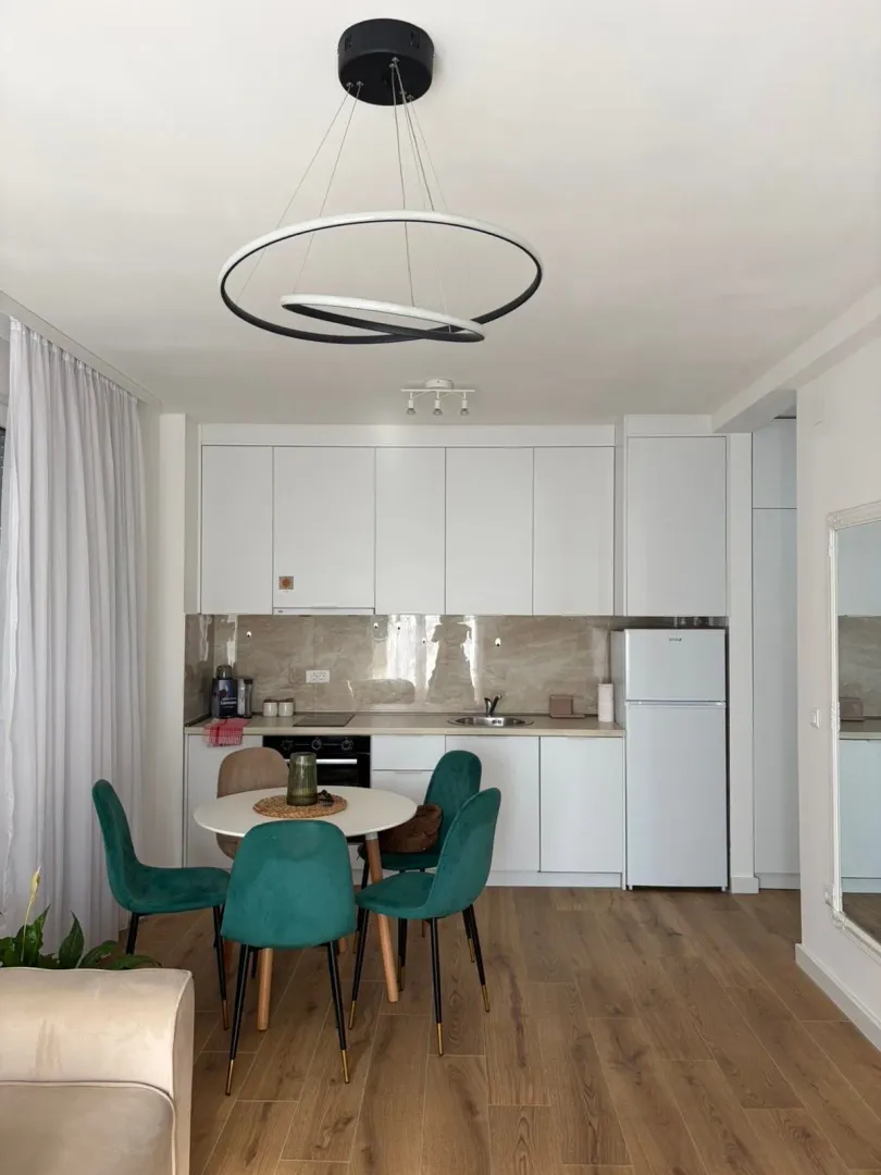 Modern white kitchen with a dining table and green chairs.