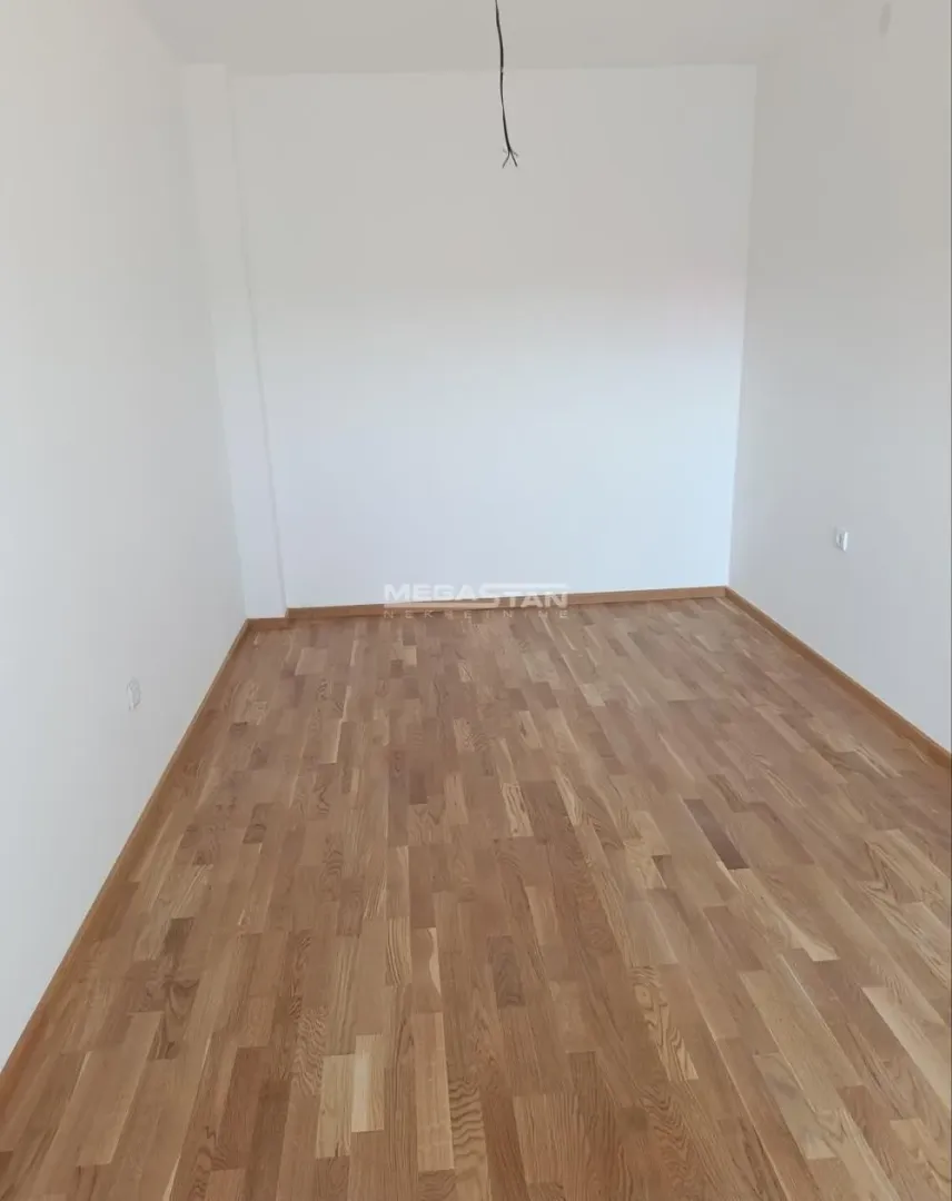 Prazna soba sa parketom na podu i belim zidovima.