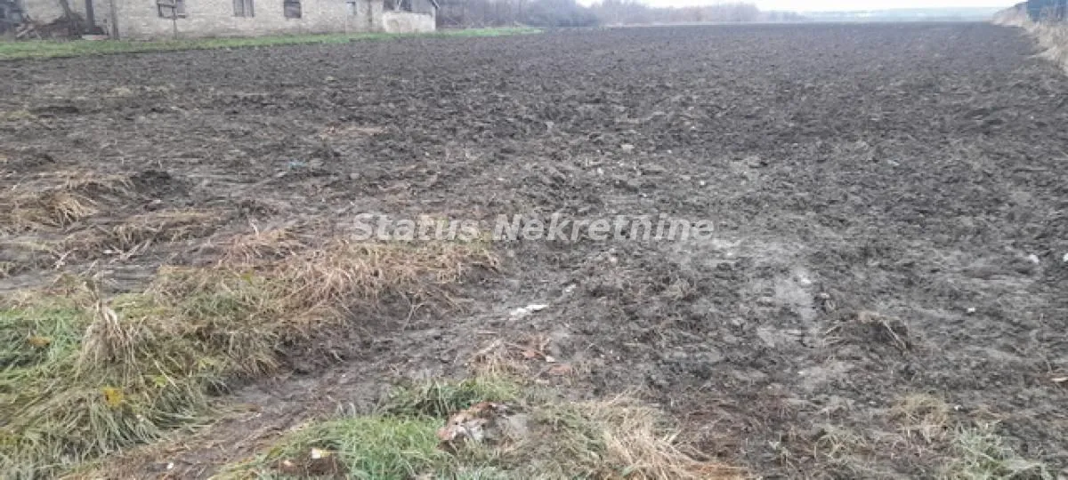 Pogled na prostrano orano zemljište sa kućom u pozadini.