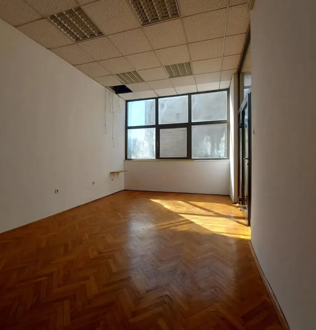 Empty office room with parquet flooring and a large window.