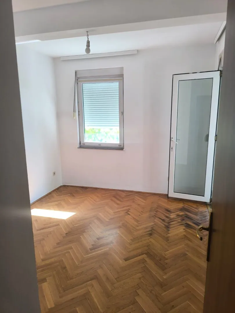 Prazna soba sa parketom i bijelim zidovima.