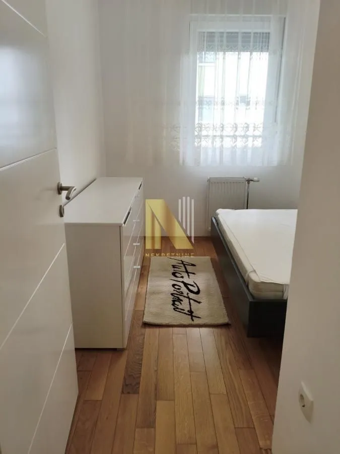Manja spavaća soba sa krevetom, komodom i drvenim podom.