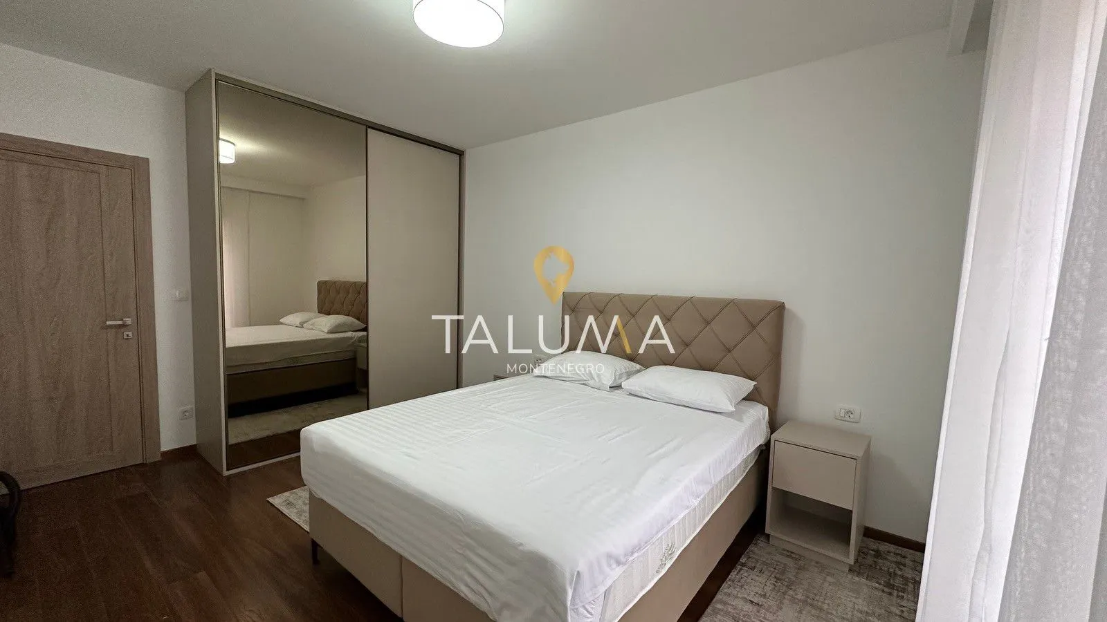 Furnished bedroom with a double bed, bedside table, and a large built-in wardrobe with a mirror.