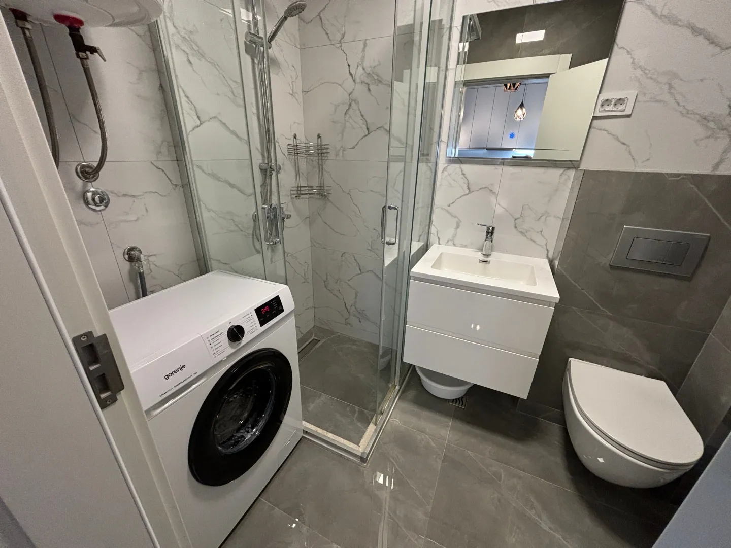 Moderne kupatilo sa tuš kabinom, umivaonikom, WC šoljom i veš mašinom.