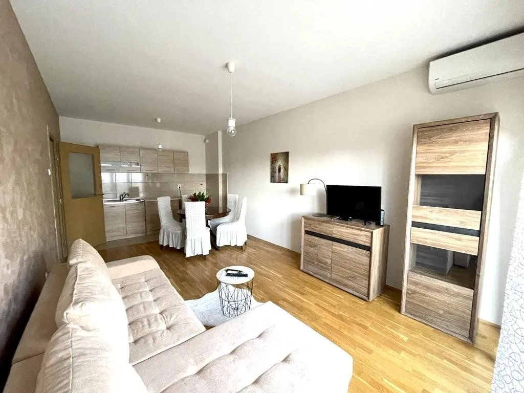 Living room with a sofa, television, and dining area in the background.