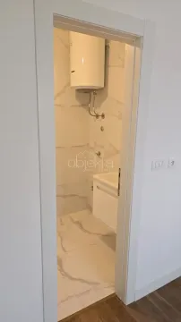 Pogled kroz vrata na kupatilo sa svijetlim mermernim pločicama i bojlerom. - image 9